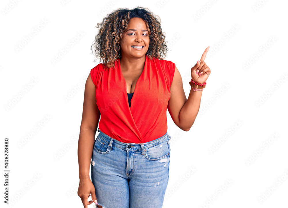 Young african american plus size woman wearing casual style with sleeveless shirt with a big smile on face, pointing with hand finger to the side looking at the camera. Young african american plus size woman wearing casual style with sleeveless shirt with a big smile on face, pointing with hand finger to the side looking at the camera.