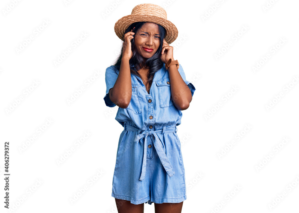 Young indian girl wearing summer hat covering ears with fingers with annoyed expression for the noise of loud music. deaf concept.