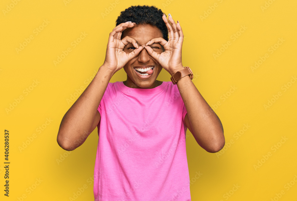 Young african american woman wearing casual clothes doing ok gesture like binoculars sticking tongue out, eyes looking through fingers. crazy expression. Young african american woman wearing casual clothes doing ok gesture like binoculars sticking tongue out, eyes looking through fingers. crazy expression.