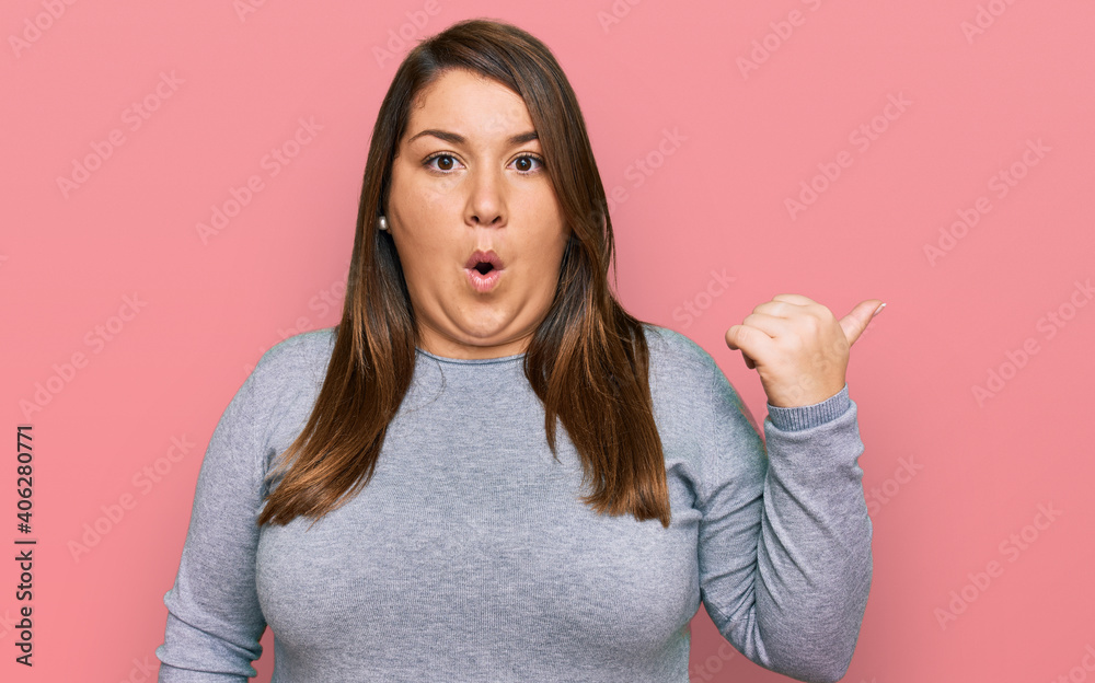 Beautiful brunette plus size woman wearing casual clothes surprised pointing with hand finger to the side, open mouth amazed expression.