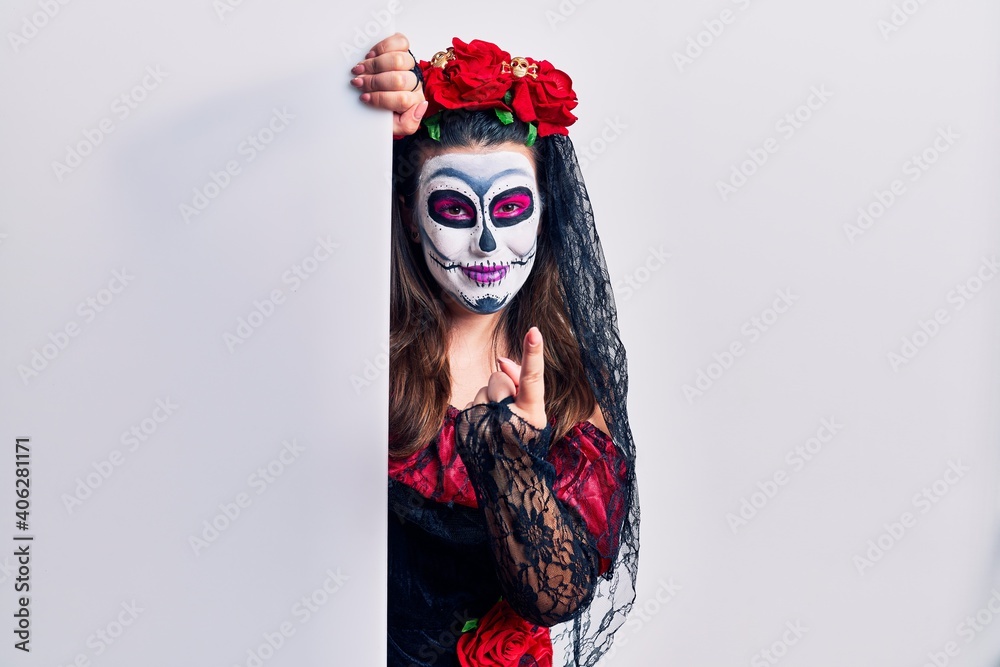 Young woman wearing day of the dead custome holding blank empty banner beckoning come here gesture with hand inviting welcoming happy and smiling