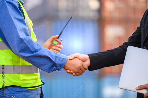 Business people and engineers Greet each other with a handshake and discuss loading container boxes from a cargo ship.