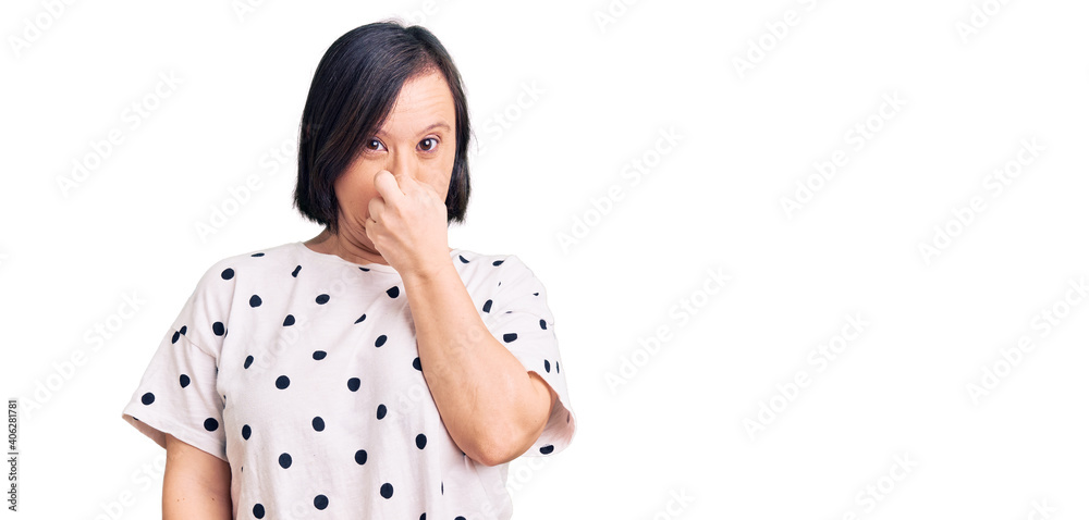 Brunette woman with down syndrome wearing casual clothes smelling something stinky and disgusting, intolerable smell, holding breath with fingers on nose. bad smell Brunette woman with down syndrome wearing casual clothes smelling something stinky and disgusting, intolerable smell, holding breath with fingers on nose. bad smell
