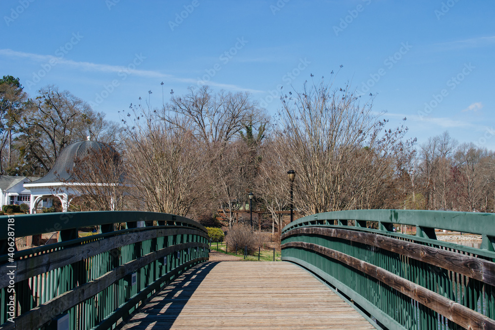 Green wooden bridge over the lake in the park in early spring on a sunny clear afternoon. Cleveland Park in Spartanburg, SC, USA on a sunny spring day.