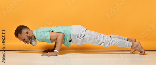 Mature bearded grey-haired man practicing yoga chaturanga push-up training studio shot full length portrait over yellow copy space. Morning or evening sport, fitness and pilates for muscle building photo