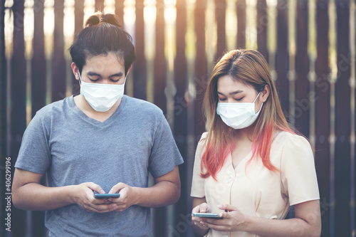 Young asia couple using smart mobile phote outdoor wearing face mask during coronavirus outbreak - Millennial couple watching videos on smartphone - Social distance and technology concept photo