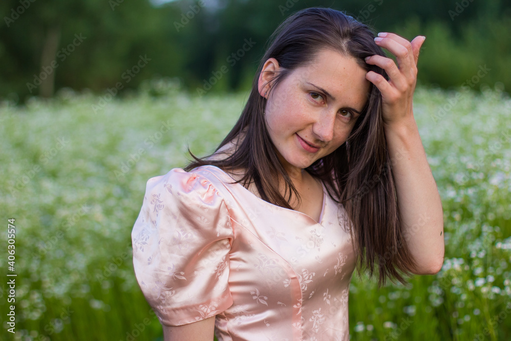 Beautiful portret of happy woman with dark hair standing in the wildflowers field in the long pink dress and sensually touching her face on a warm summer evening. Joyfull summer walking. Beautiful portret of happy woman with dark hair standing in the wildflowers field in the long pink dress and sensually touching her face on a warm summer evening. Joyfull summer walking.