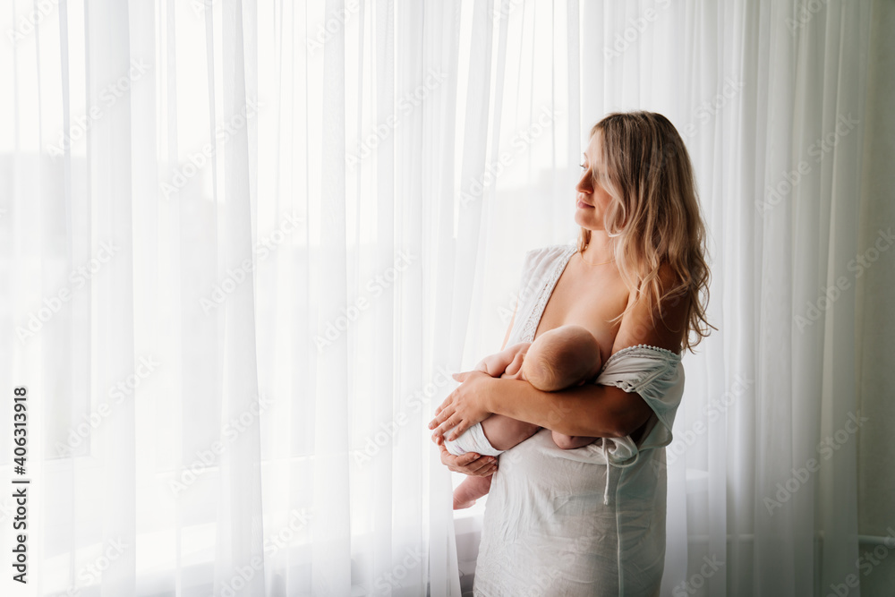 mom feeds baby standing at the window. breast-feeding. mom feeds baby standing at the window. breast-feeding.
