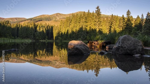 4K Time Lapse of Beautiful landscape with mountains illuminated, reflection in mountain lake, blue sky and yellow sunlight. Slovakia, Vrbicke Pleso Low Tatras photo