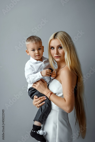 Fashion mom in a white elegant outfit and a baby on a gray background. Feminism concept, mother's day.