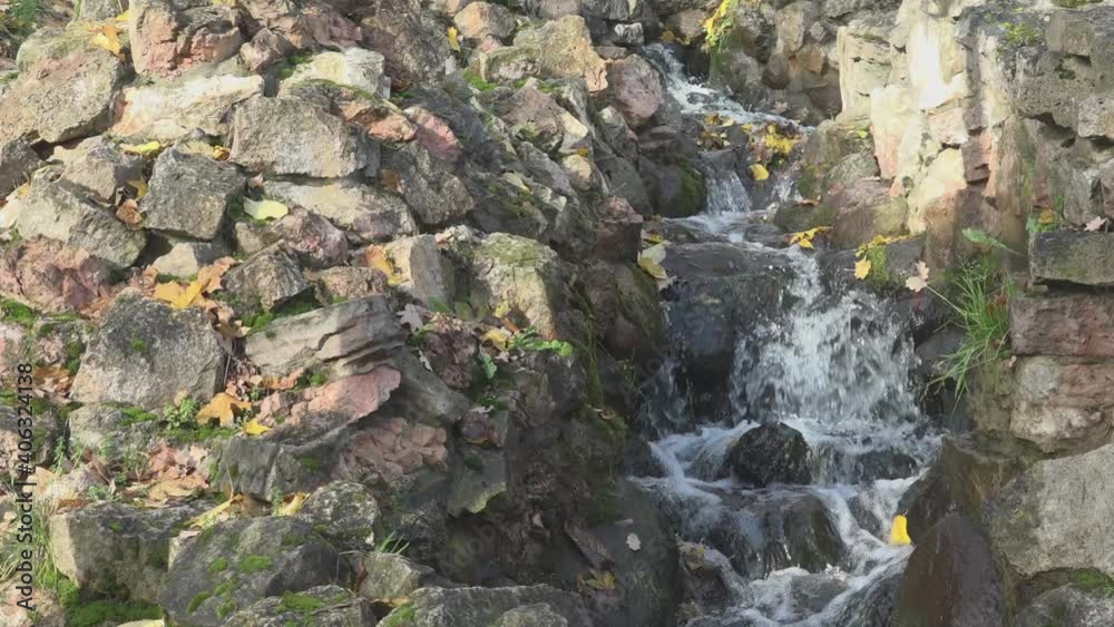 Stream with waterfall and rapids runs down among large brown stone pile located in beautiful autumn Riga Bastejkalns city park Stream with waterfall and rapids runs down among large brown stone pile located in beautiful autumn Riga Bastejkalns city park