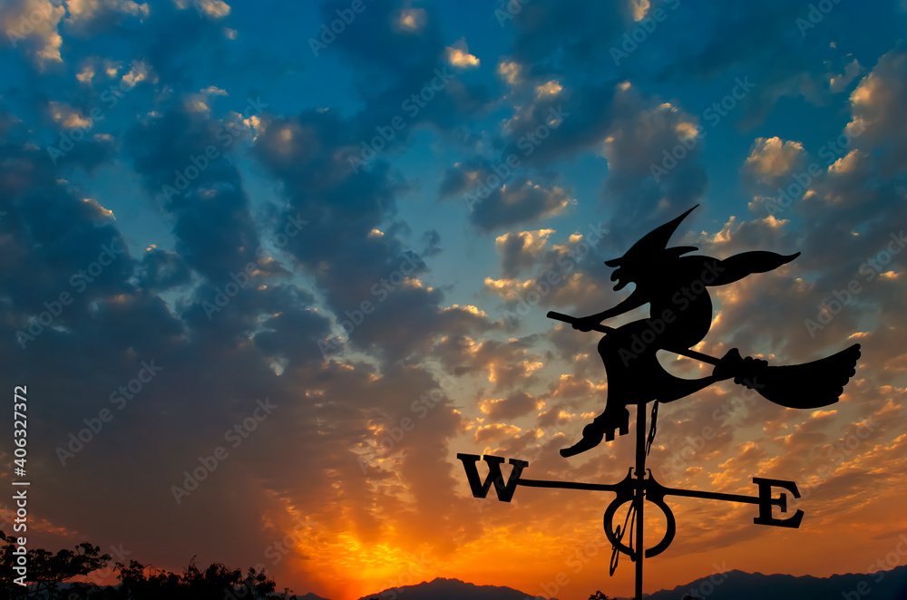 Silhouette of weather vane with witch flying on broomstick, dramatic sky and colorful clouds at dawn above mountains. Concept of weather forecasting Silhouette of weather vane with witch flying on broomstick, dramatic sky and colorful clouds at dawn above mountains. Concept of weather forecasting