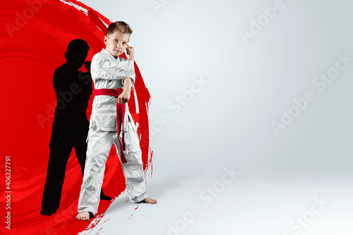 A boy in a white kimono with a red belt against the background of a red circle, the sun. Karate concept, goal, training, achievement.
