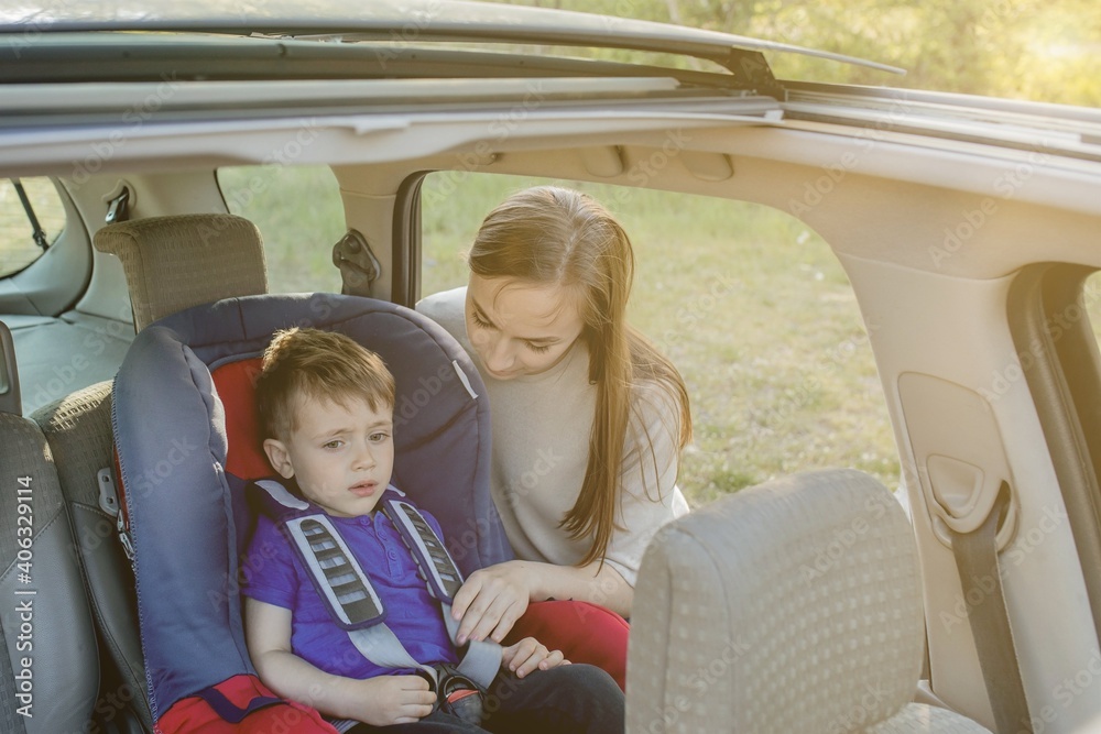 Fototapeta premium Mother gives the phone little boy sitting in a car seat. Safety of transportation of children.