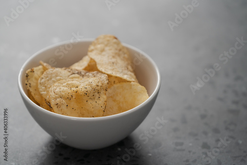 White bowl with organic potato chips sprinkled with fresh ground black pepper on concrete background with copy space