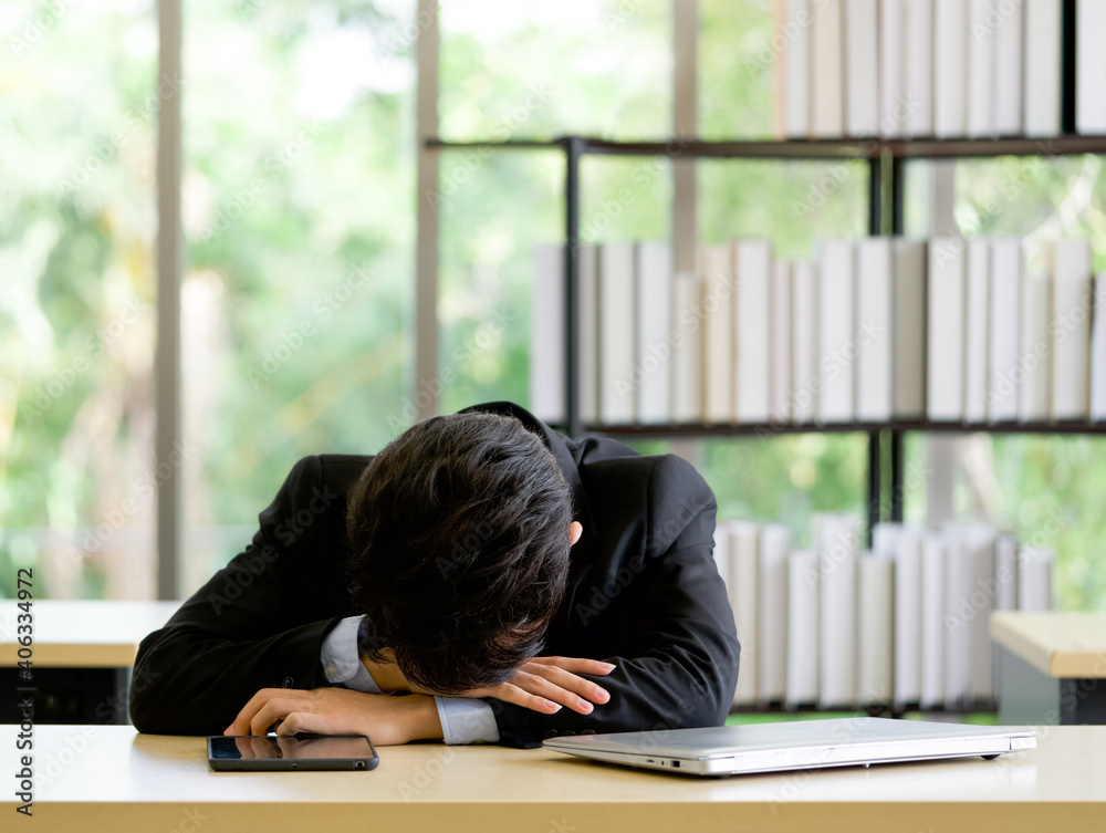 Young asian employee take a nap in the office on a table with tablet and laptop computer. Young asian employee take a nap in the office on a table with tablet and laptop computer.