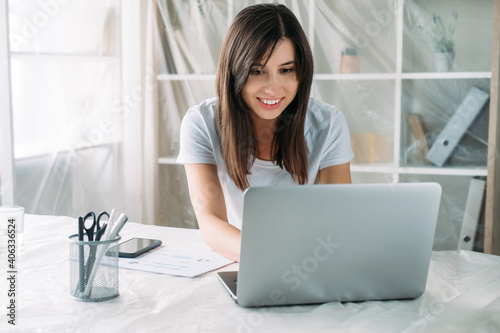 Freelancer lifestyle. Home relocation. Remote job. Virtual office. Happy satisfied woman working online using laptop in new modern light room with covered furniture. photo