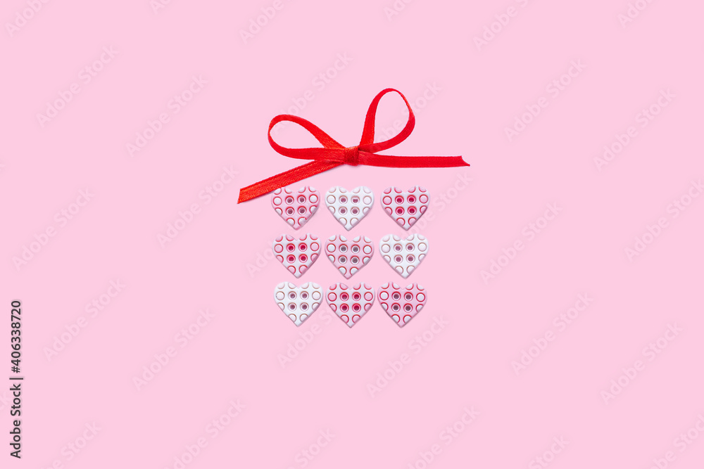 Gift box for beloved. Gift box made of tiny buttons hearts with bright red ribbon bow isolated on pink background. Present for a loved one on Valentine's day.