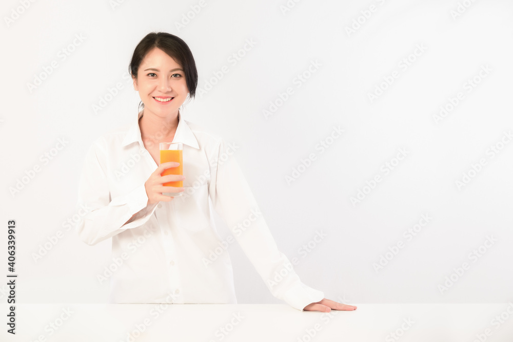 Asian young woman wearing white shirt is holding a glass of natural orange juice on white background with copy space. Asian young woman wearing white shirt is holding a glass of natural orange juice on white background with copy space.