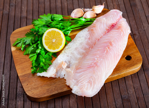Fotografie Raw fish with condiments, perch fillet with garlic, parsley and lemon on wooden
