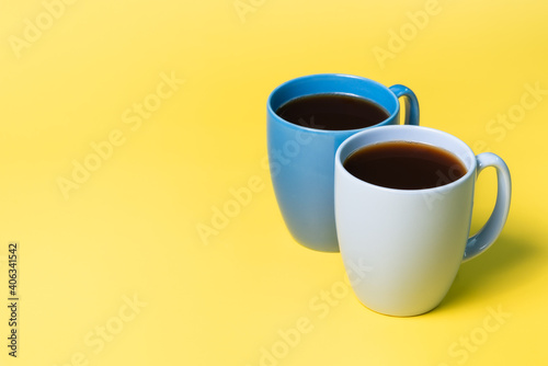 Two coffee mugs on a yellow background.