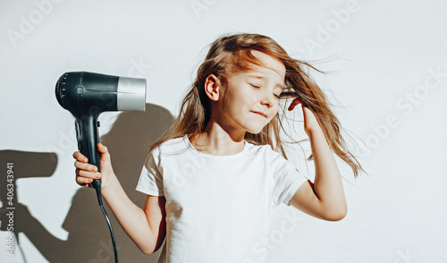 Girl in white t-shot dries her hair with a hair dryer