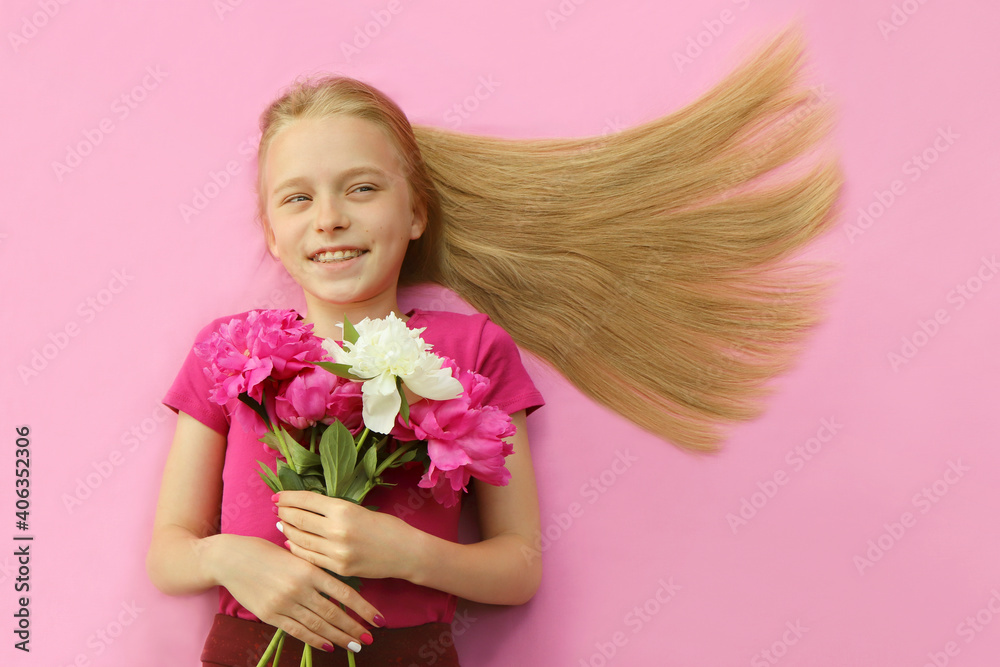 A girl with peonies, beautiful blonde hair and a colorful children's manicure on a pink background.Fashion nail art and hairstyle. A girl with peonies, beautiful blonde hair and a colorful children's manicure on a pink background.Fashion nail art and hairstyle.