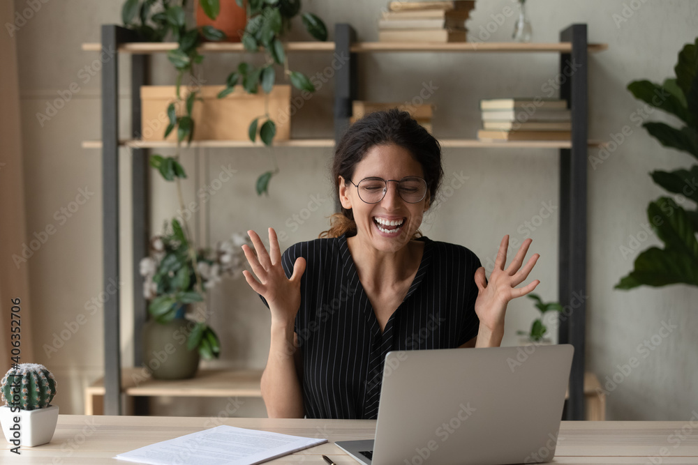 Excited young Caucasian woman in glasses sit at desk at home office look at laptop screen triumph get promotion email letter. Happy millennial female feel euphoric with good news online on computer. Excited young Caucasian woman in glasses sit at desk at home office look at laptop screen triumph get promotion email letter. Happy millennial female feel euphoric with good news online on computer.
