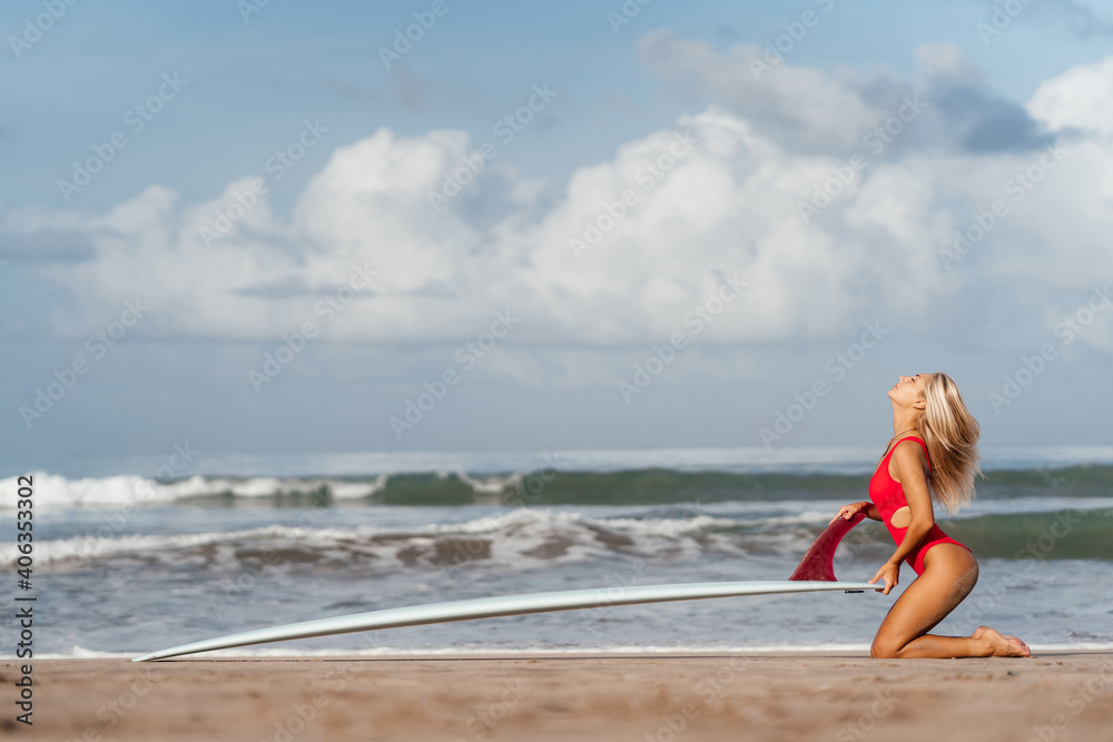 Naklejka premium Surf woman with long blonde hair go to ocean. Female holding surfboard ready to surf. Bali island, Indonesia. Outdoor Active Lifestyle.