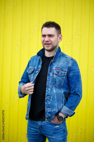 Portrait of a handsome stylish guy, a man dressed in a black blank t-shirt standing on a yellow wall background. Urban style of clothes, modern fashionable image. Men's fashion