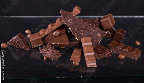 Broken chocolate pieces and cocoa powder on wooden background.