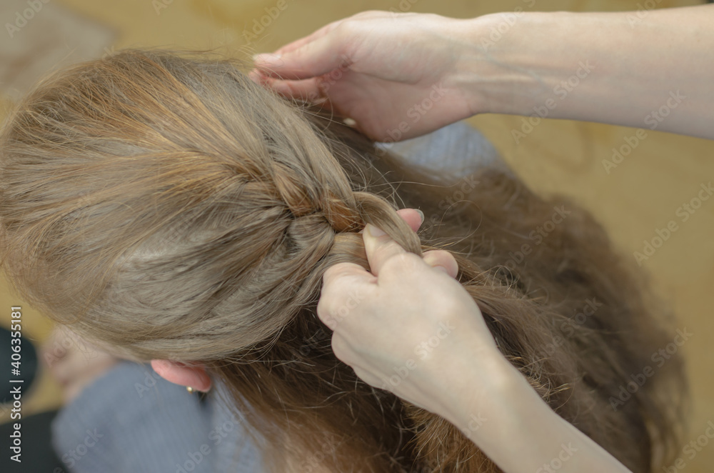Fototapeta premium A woman braids a pigtail for a red-haired girl. Hair weaving hairstyles. Braiding close up