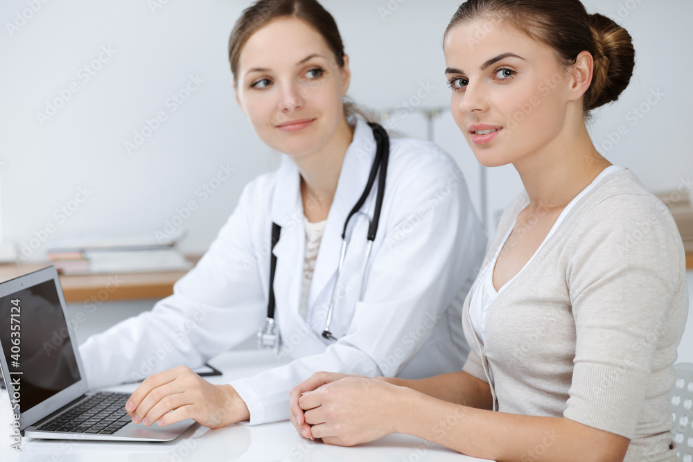 Doctor and patient are sitting and discussing health examination results while using laptop computer. Health care, medicine and good news concepts Doctor and patient are sitting and discussing health examination results while using laptop computer. Health care, medicine and good news concepts