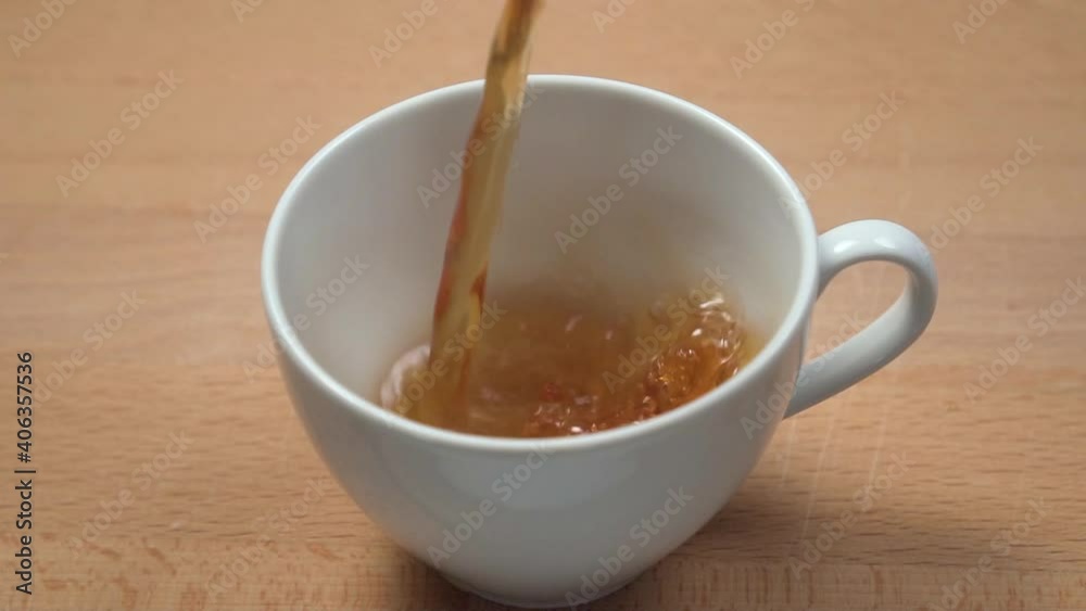 Pouring brewed black tea into a white cup close-up on a wooden table. Slow motion. Tea time concept Pouring brewed black tea into a white cup close-up on a wooden table. Slow motion. Tea time concept