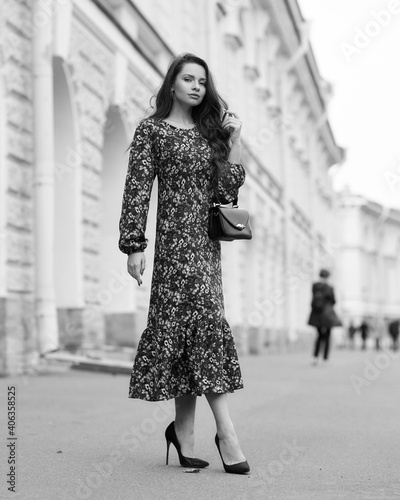 Elegant woman in dress walking city street on fall or autumn day. Pretty girl with long wavy hair holding handbag