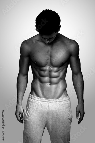 Front portrait of a handsome brunette man with muscular body posing at studio, looking down. Black and white photo.