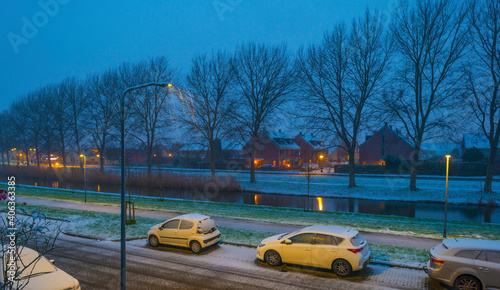 First snow at night in a residential street with parked cars along a canal in winter  Almere  Flevoland  The Netherlands  January 16  2020