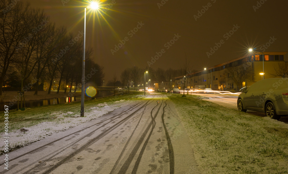 First snow at night in a residential street with parked cars along a canal in winter, Almere, Flevoland, The Netherlands, January 16, 2020