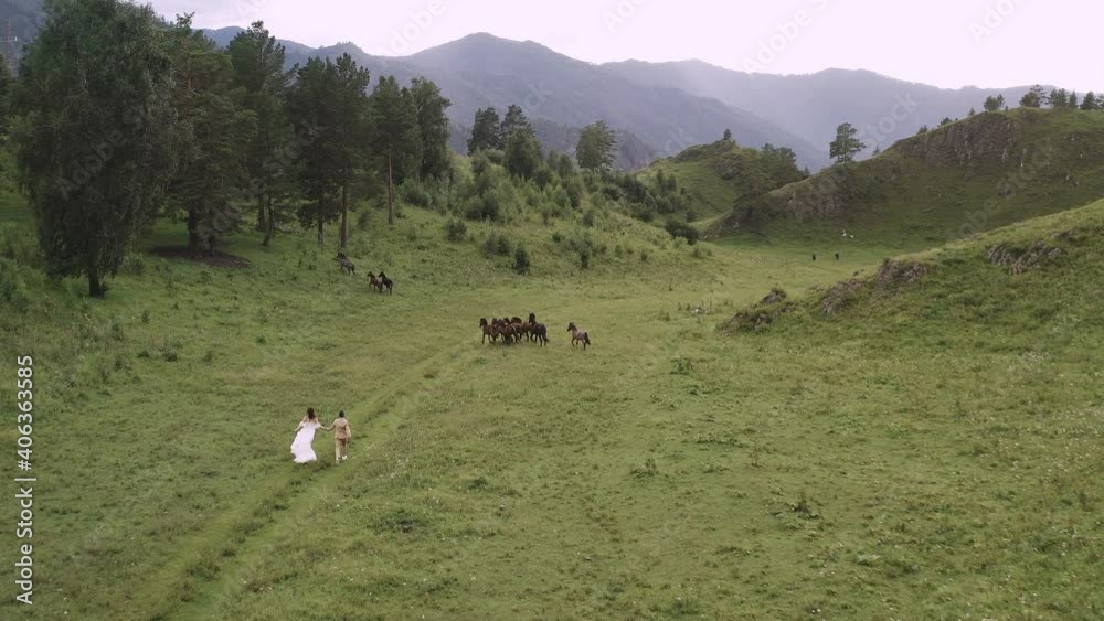 The bride and groom in a dress go to a herd of horses against the background of mountains in Altai The bride and groom in a dress go to a herd of horses against the background of mountains in Altai