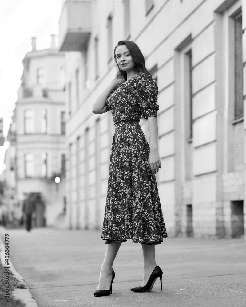 Elegant caucasian brunette woman with long wavy hair in midi green dress with floral print walking at city street on autumn day