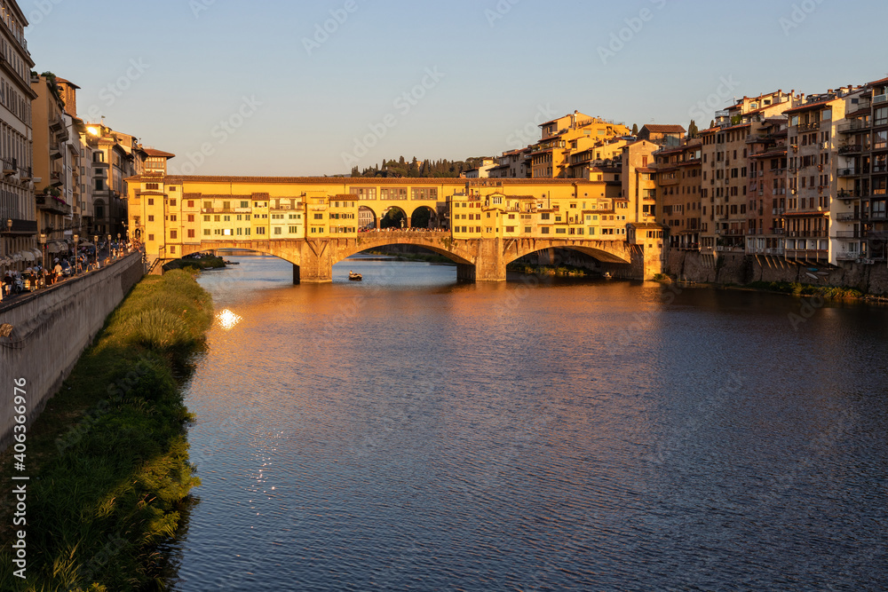 a boat with tourists sails under the famous Ponte Vecchio bridge over the Arno river