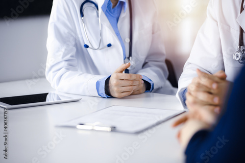 Two doctors and patient woman discussing something while sitting at the desk in modern clinic. Perfect medical service, medicine concept