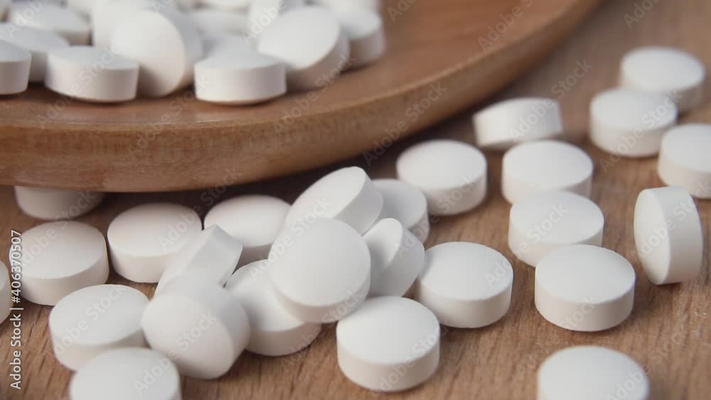 White pills fall on a wooden surface in slow motion next to a wooden spoon. Macro. Natural food supplements concept White pills fall on a wooden surface in slow motion next to a wooden spoon. Macro. Natural food supplements concept