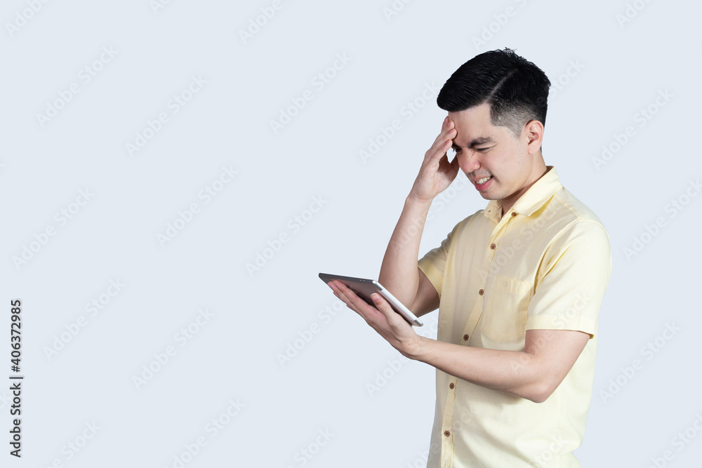 Terrible headache. portrait handsome young asian man wearing a yellow shirt holding smart phone or tablet feeling stressful isolated on white background. Businessman concept. Asia people. Terrible headache. portrait handsome young asian man wearing a yellow shirt holding smart phone or tablet feeling stressful isolated on white background. Businessman concept. Asia people.