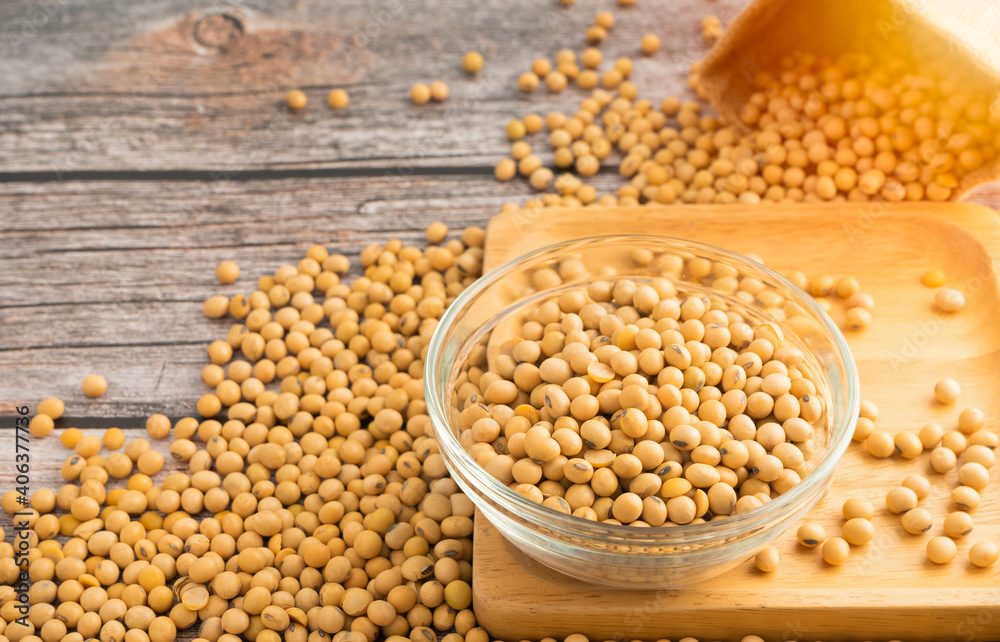 Soybeans in glass bowl with Soybeans pour from bag on wooden table background.Healthy food Concept.