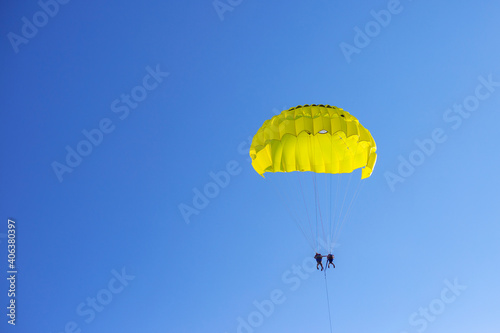 Yellow parachute with people in the blue sky. Paragliding in the sky