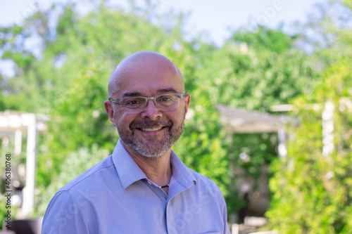 Portrait of a senior man.  Elderly bald man with beard in a blue shirt and glasses is smiling in a summer park