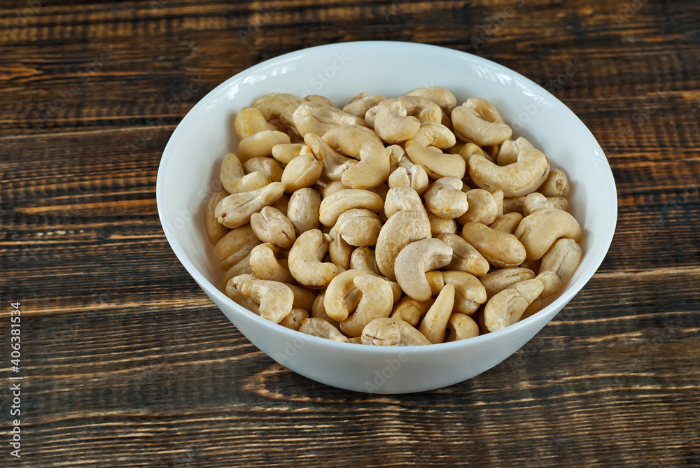 Cashews in a white bowl on an old shabby board. Nuts on a brown wooden table. Cashews in a white bowl on an old shabby board. Nuts on a brown wooden table.