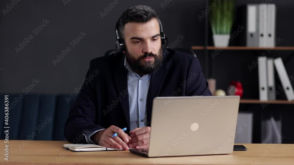 Handsome bearded man studying online using laptop web camera, writing lecture in notebook.Online education, remote working, home education.Online meeting, video call, video conference, courses online