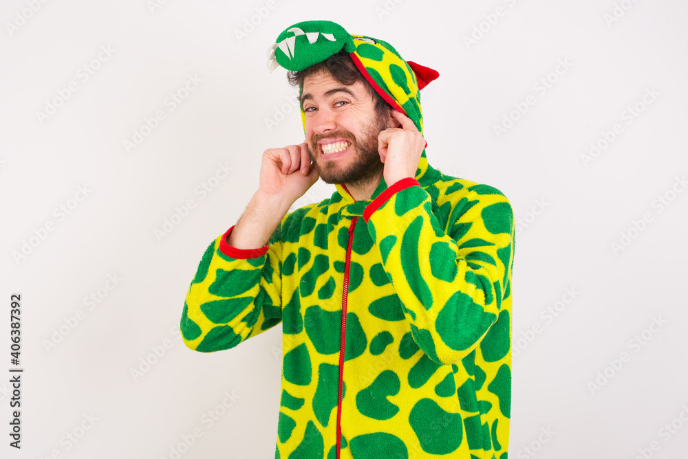 Young caucasian man wearing a pajama standing against white background covering ears with fingers with annoyed expression for the noise of loud music. Deaf concept.